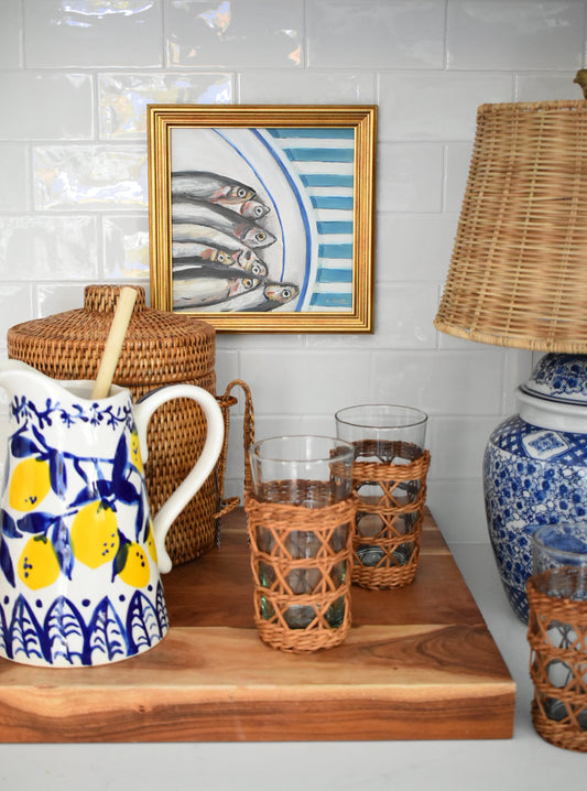 Decorative setting with wicker basket, blue and white ceramic items, and framed artwork on a tiled wall.